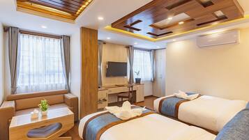 A hotel room with two beds, a desk, a chair, a TV, and a window with curtains.