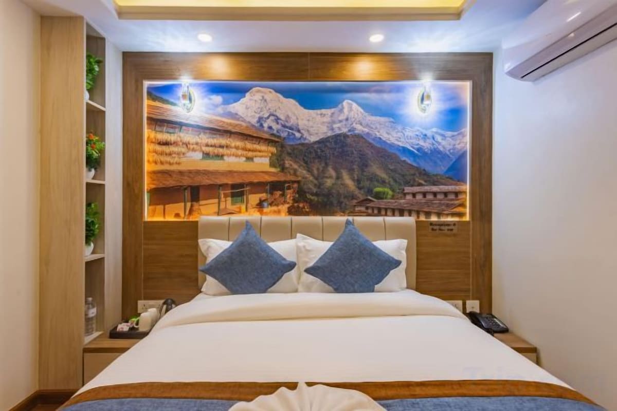 Una habitación de hotel con una cama grande, cabecera de madera y un cuadro colgado en la pared que muestra un paisaje montañoso.