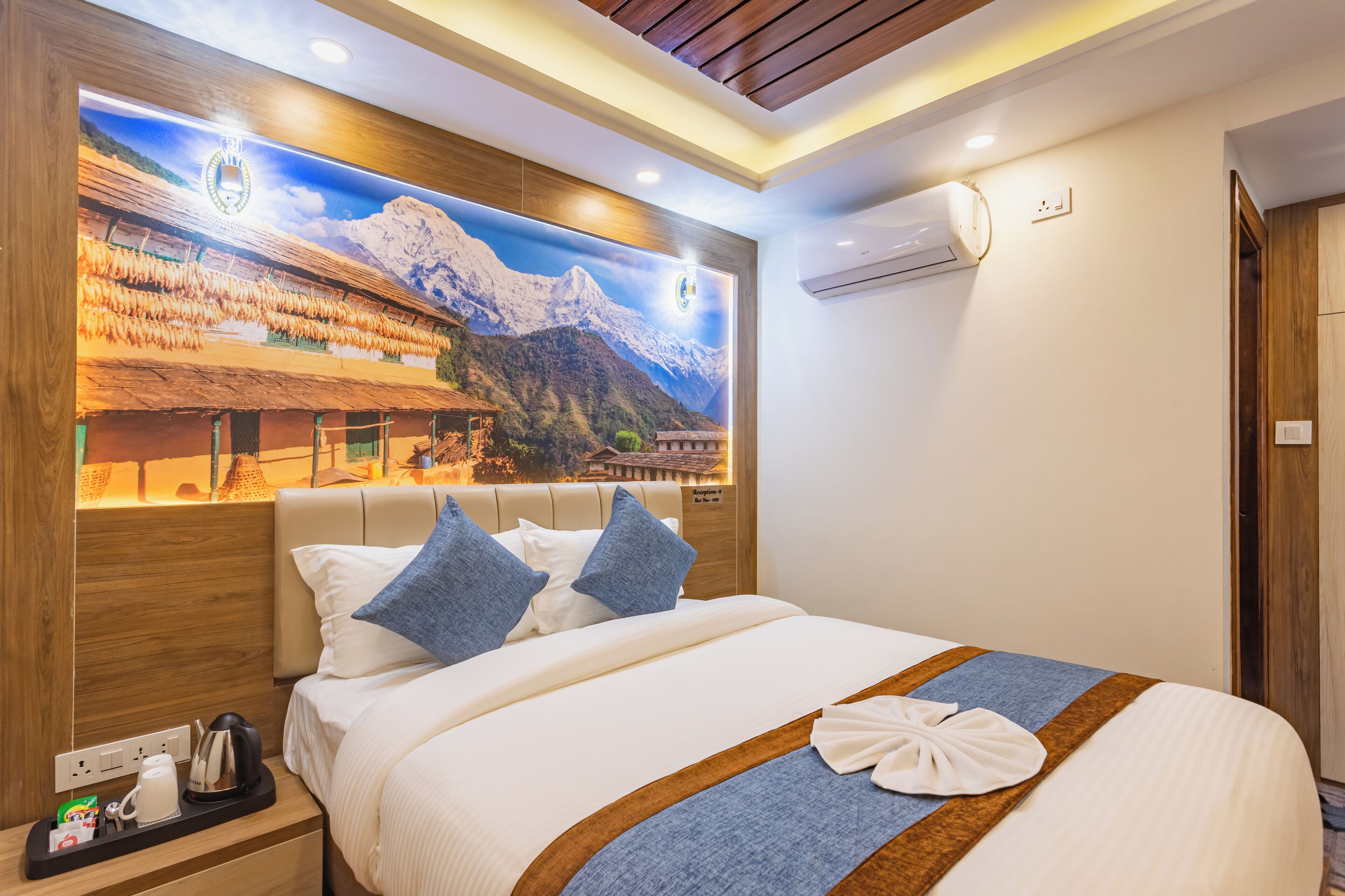 A hotel room with a large bed, a nightstand with a kettle, and a wall-mounted air conditioner.