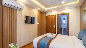 A modern hotel room with a large bed, a mounted TV, a wooden panel wall, and a built-in sink.