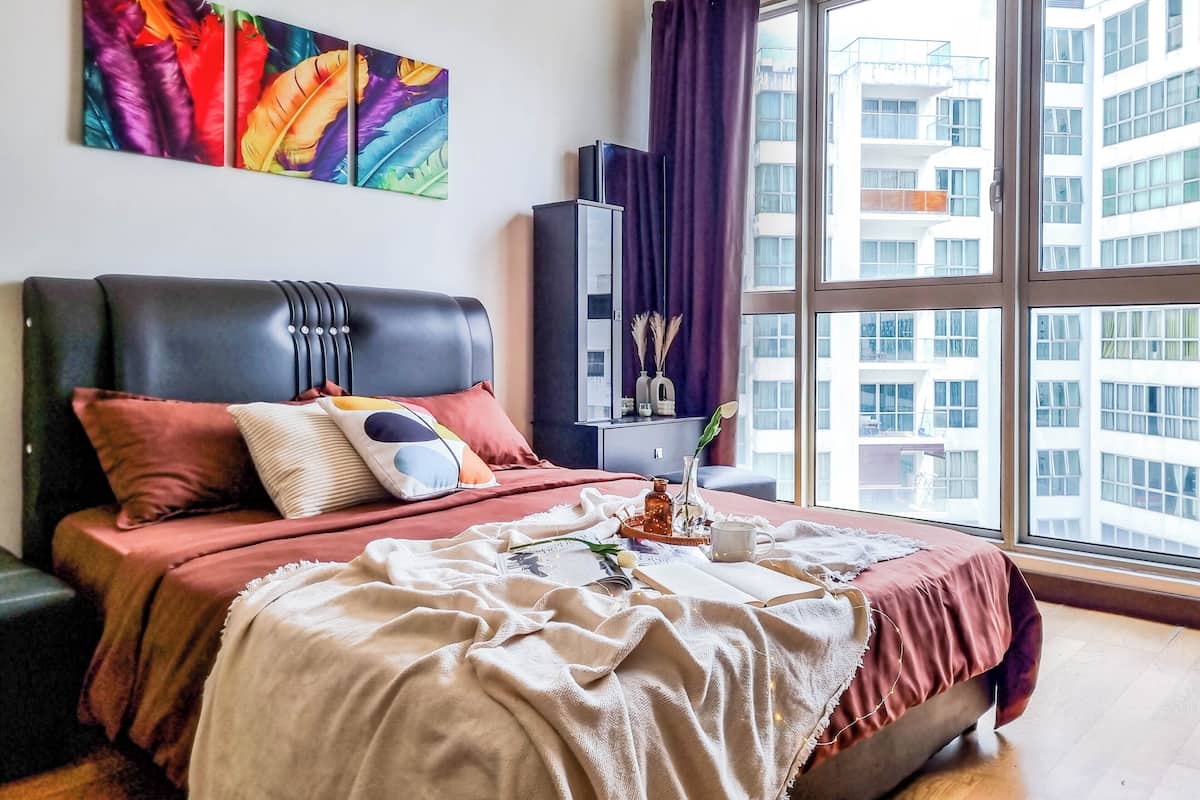 Une chambre à coucher moderne avec une grande fenêtre, une tête de lit en cuir noir et un tableau abstrait aux couleurs vives.