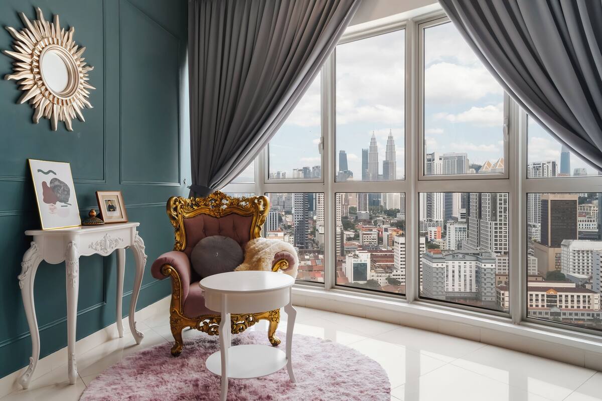 Ein Zimmer mit großem Fenster, einem bequemen Sessel, einem kleinen Tisch und einem dekorativen Spiegel.