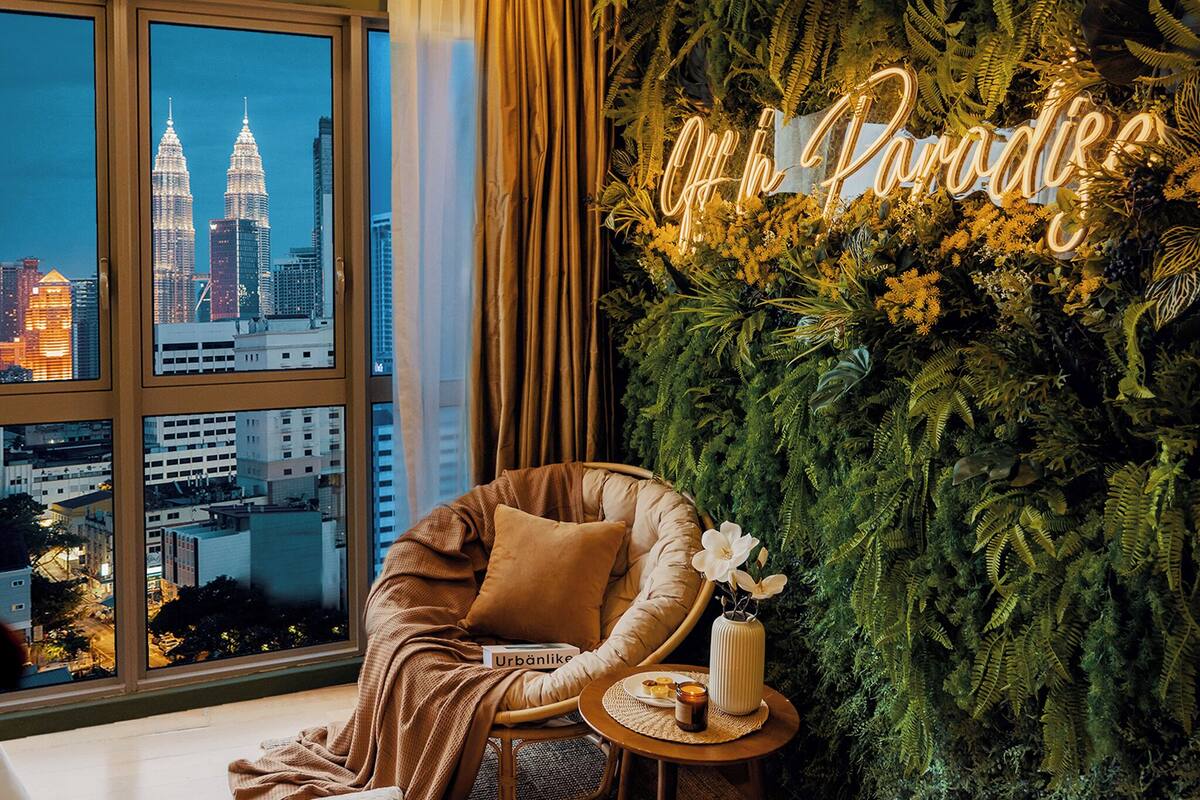 Une chambre avec vue sur les tours Petronas, un fauteuil confortable, une petite table avec une bougie et un panneau indiquant « Paradis ».