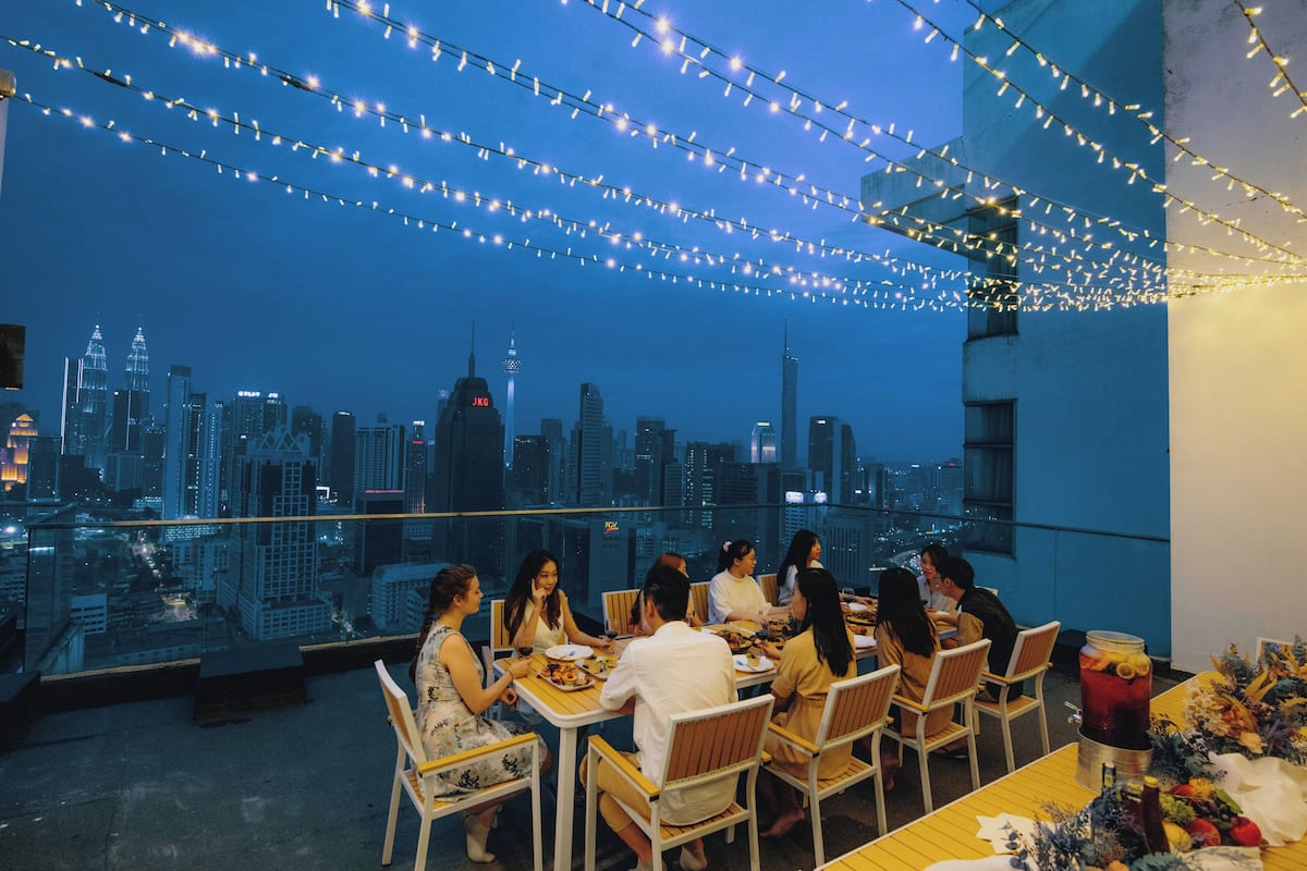 Un espace de restauration aménagé sur le toit, offrant une vue sur la ville, illuminé de guirlandes lumineuses et doté de tables préparées pour le repas.