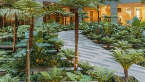 A modern building with multiple floors, large windows, and a central courtyard with various plants and a pathway. - NaiBnB @ Regalia Residence (Kuala Lumpur)