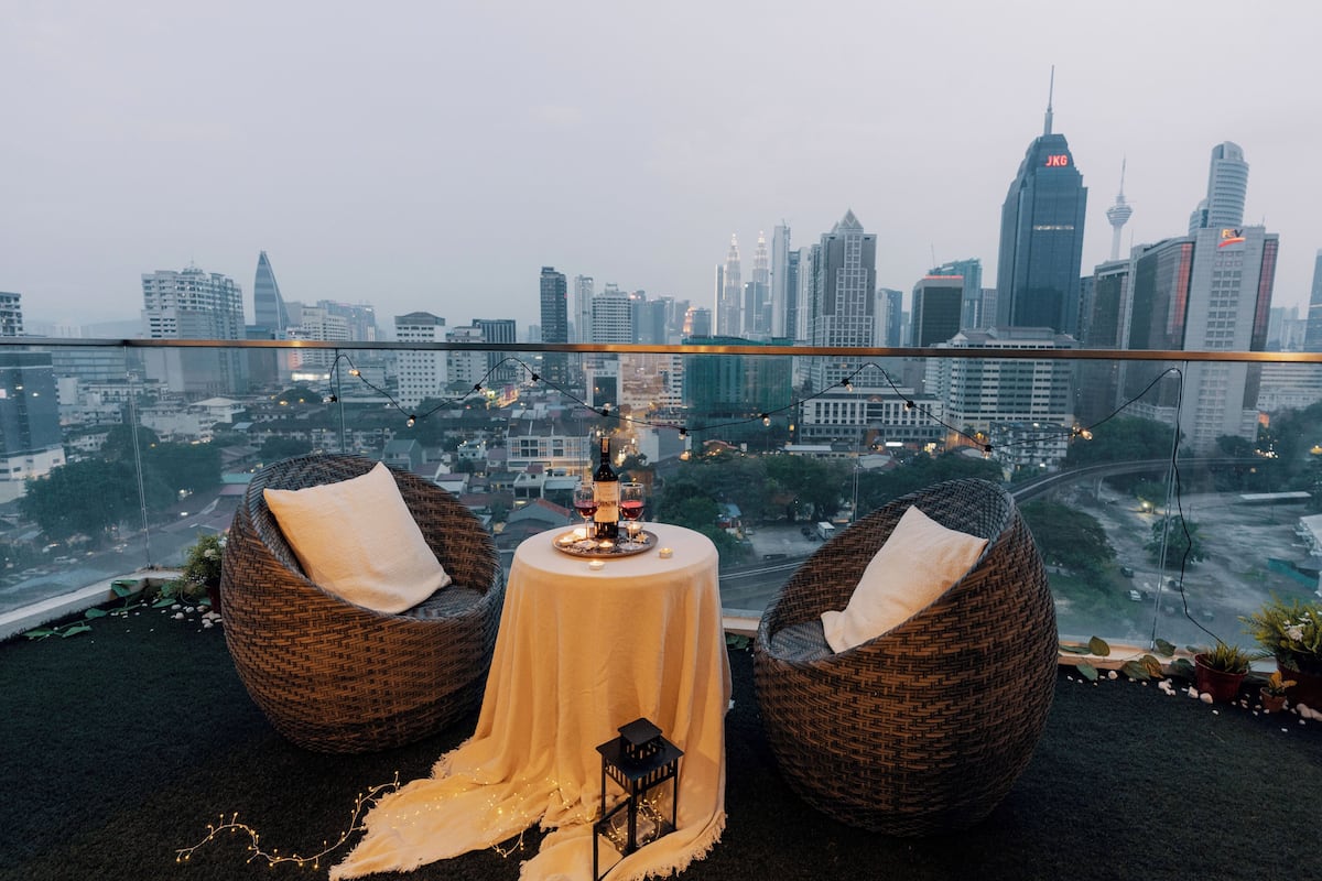 Une terrasse sur le toit, avec des fauteuils en osier, une table avec une bougie et une vue imprenable sur les toits de la ville.