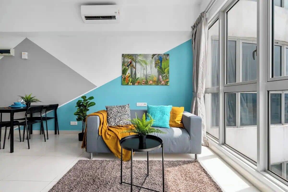 Un salon moderne avec un canapé gris, une table basse noire et un tableau représentant un paysage tropical.