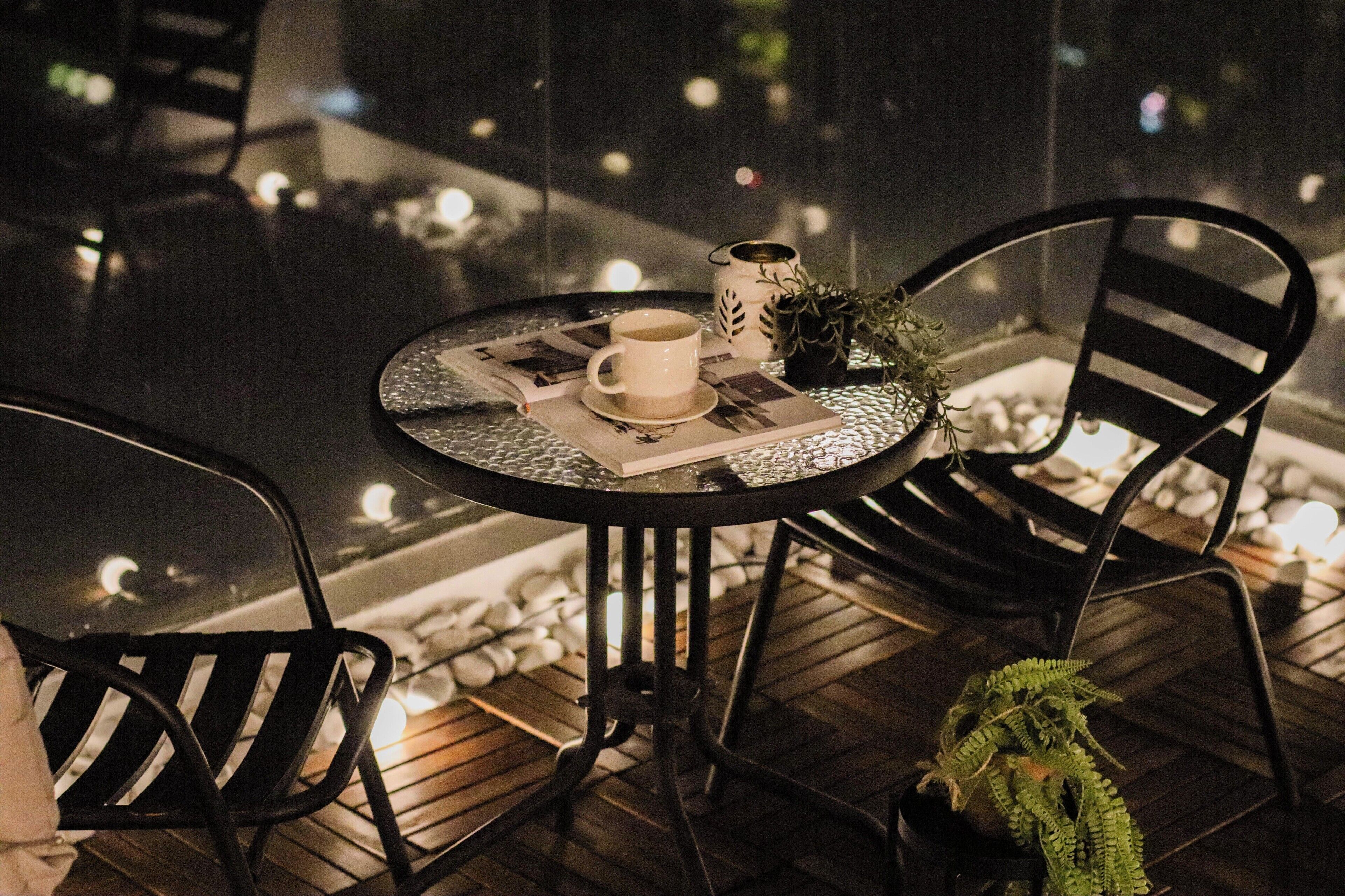 A round table with a cup, saucer, and a small plant. There are two chairs around the table.