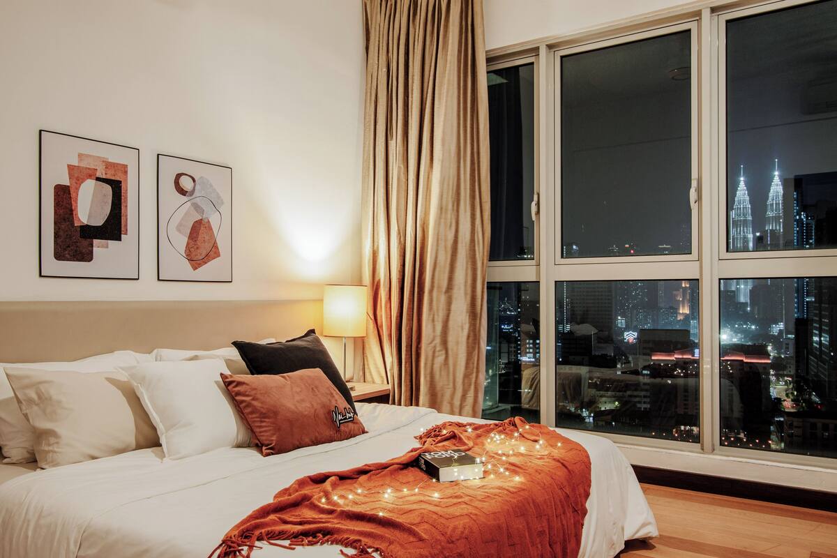 Une chambre d’hôtel avec un lit, une fenêtre donnant sur la ville et deux œuvres d’art encadrées accrochées au mur.