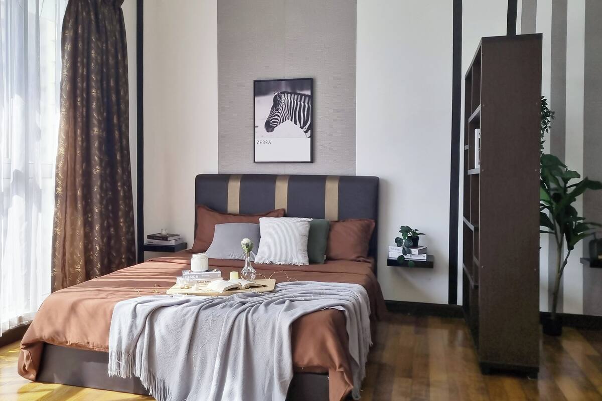 Ein modernes Schlafzimmer mit einem großen Bett, einem Nachttisch mit Lampe, einem Bilderrahmen mit Zebra-Motiv an der Wand und einer Zimmerpflanze.