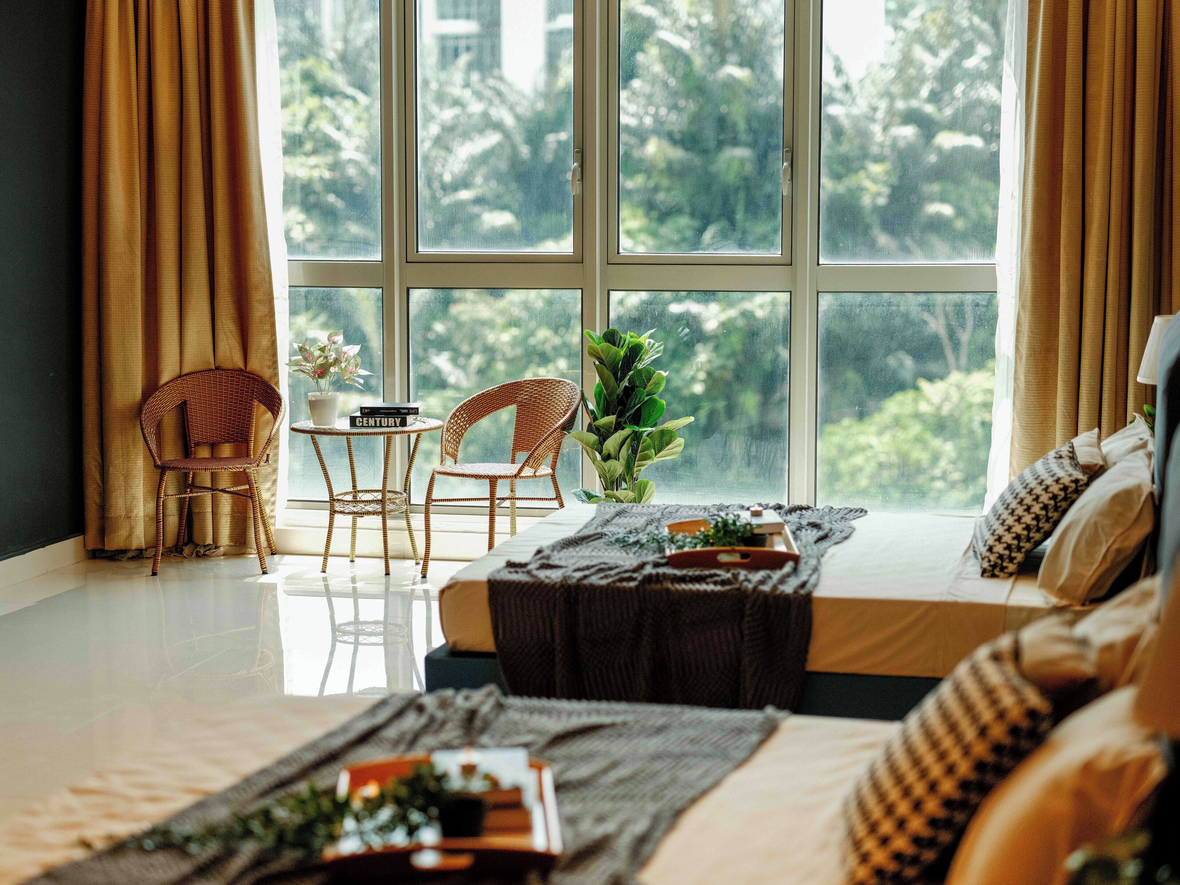Una habitación con un ventanal grande, una cama, una silla, una mesita con un libro y una planta.