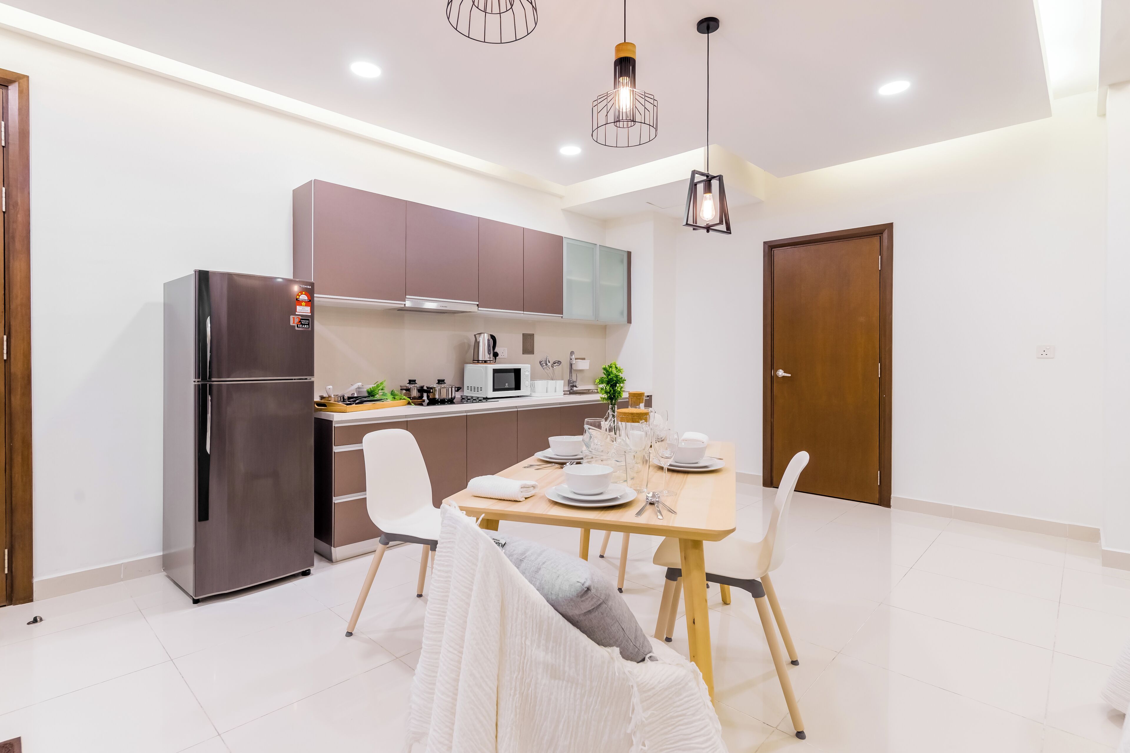 A modern kitchen with stainless steel appliances, a dining area with a wooden table and white chairs, and pendant lighting.