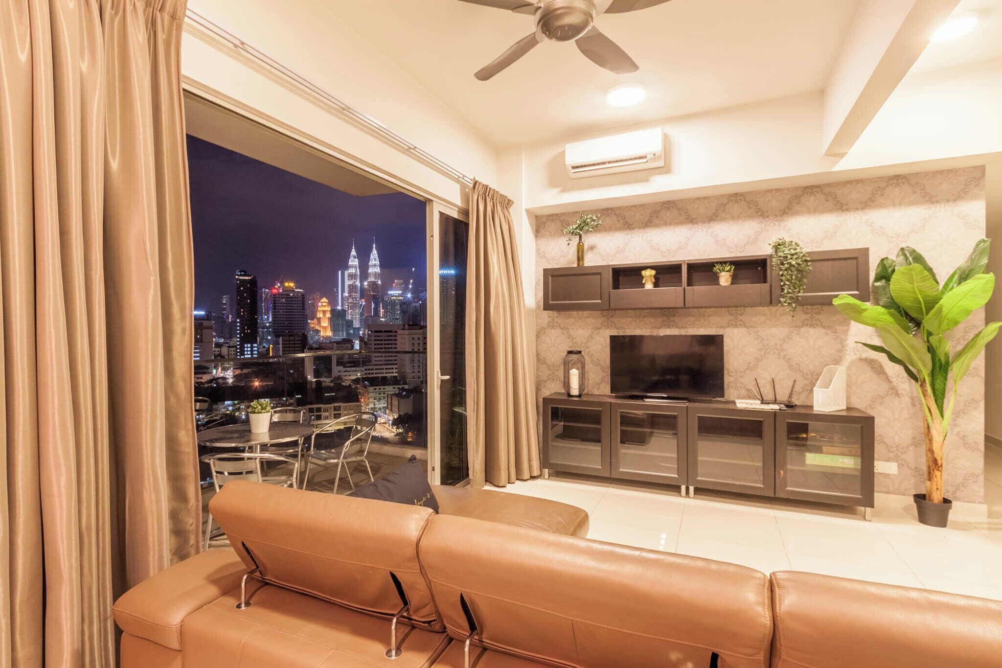 A modern living room with a large TV, a ceiling fan, and a view of a cityscape at night.