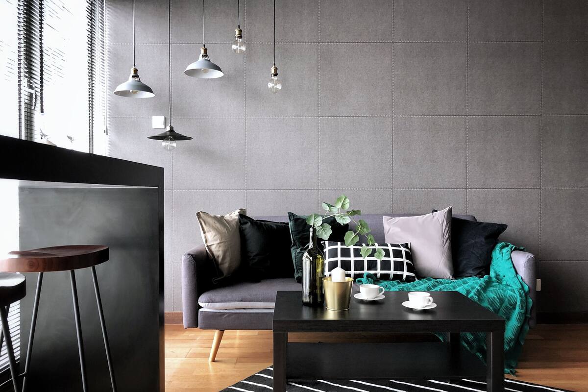 Un salon moderne avec un canapé gris, une table basse noire et des lampes suspendues.