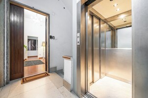 Vista interior de un vestíbulo de hotel con una puerta de madera, una recepción y un ascensor moderno.