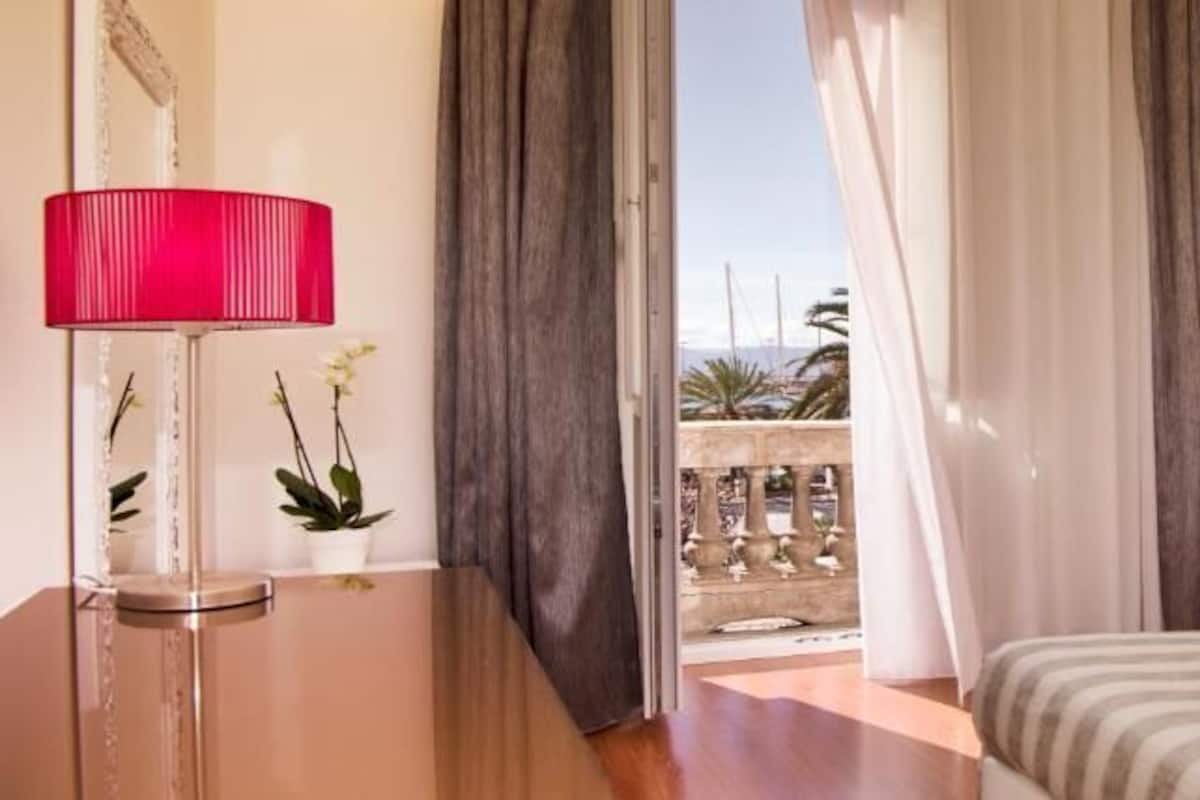 A hotel room with a bed, a red lamp, a potted plant, and a view of the outside balcony.