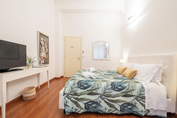 A bedroom with a bed, a TV, a desk, and a door. - Blanco Rooms (Cagliari)