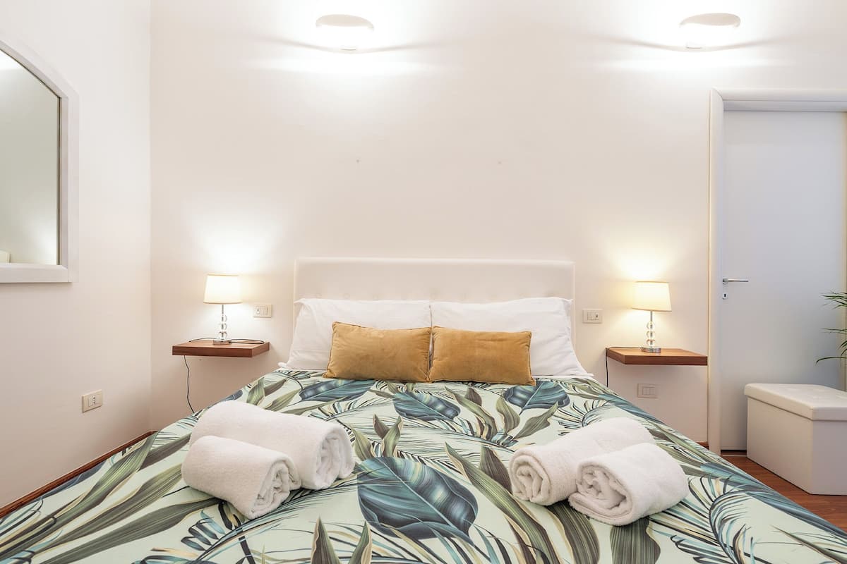 A hotel room with a bed, two bedside lamps, a nightstand, a mirror, and a door.