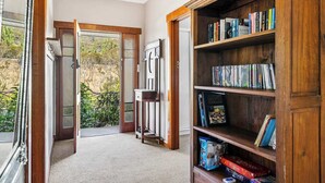 A room with a wooden bookshelf, a door leading to a balcony, and a view of greenery outside. - "Cascade Cottage" South Hobart with parking (South Hobart)