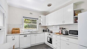 A modern kitchen with white cabinetry, a built-in oven, a microwave, and a window with a view of greenery. - "Cascade Cottage" South Hobart with parking (South Hobart)