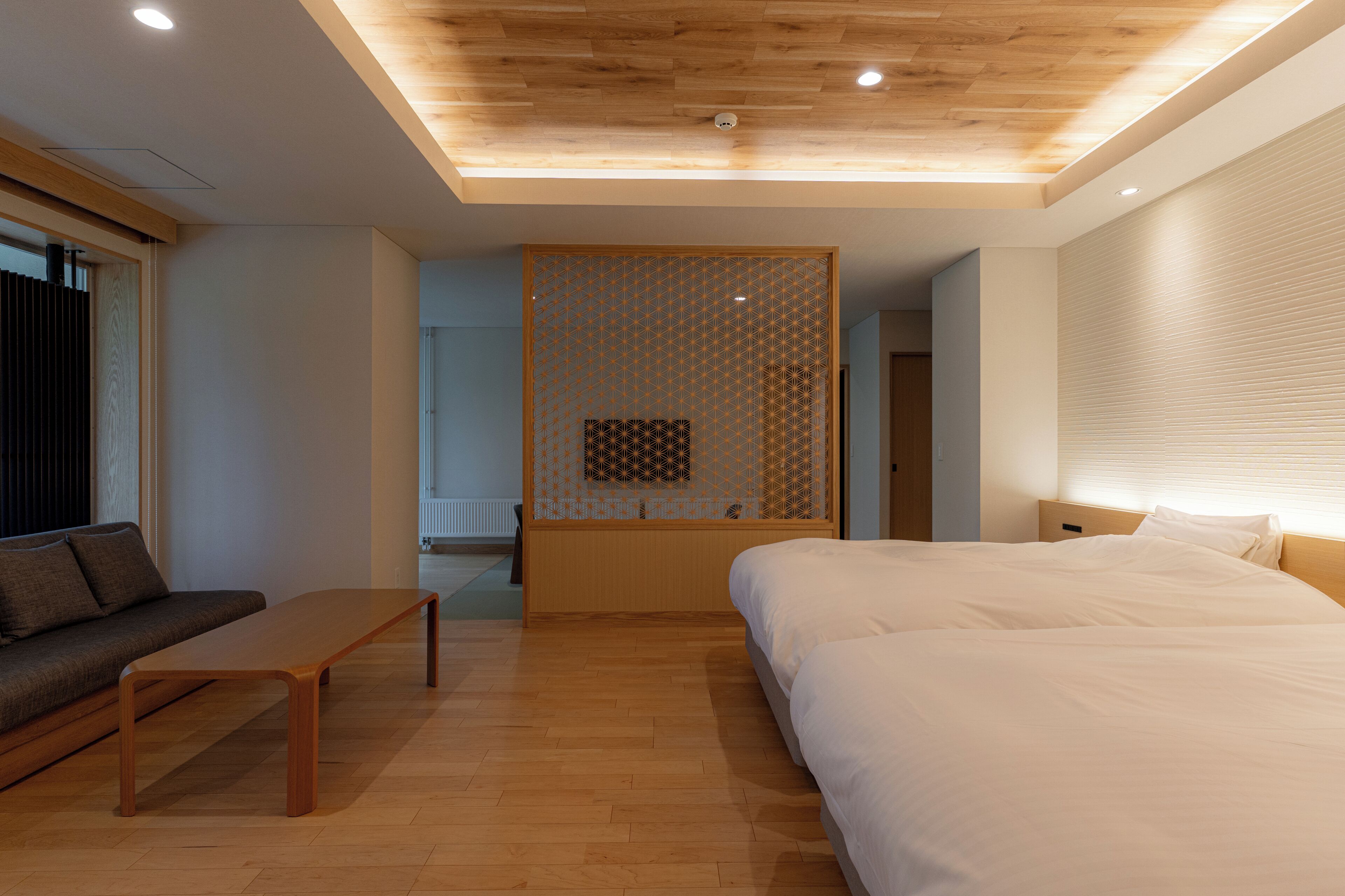 A modern hotel room with a wooden ceiling, a bed, a sofa, and a small table.
