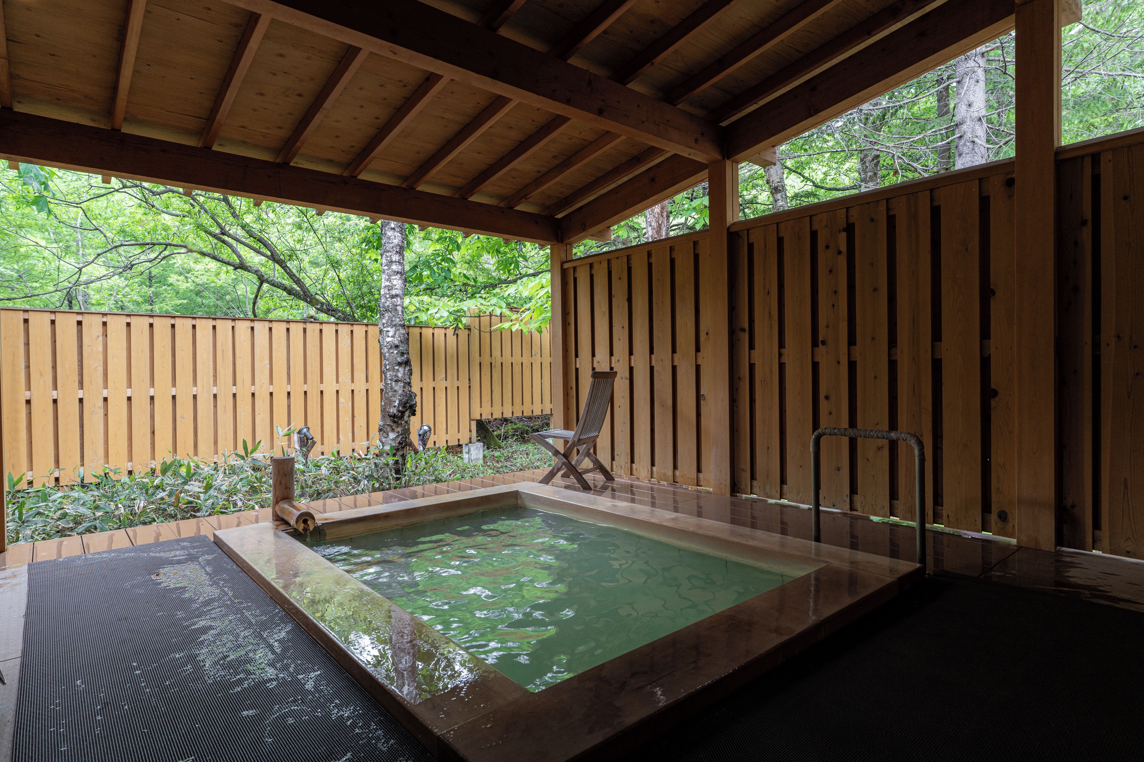 Una terraza de madera con un jacuzzi, una silla y una escalera de metal.