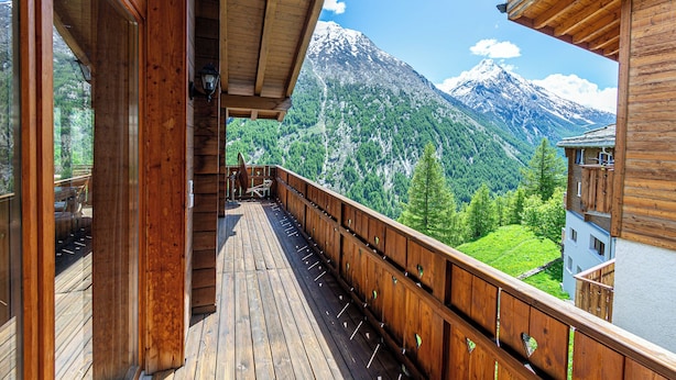 Un balcon en bois offrant une vue sur une montagne enneigée et une végétation luxuriante.