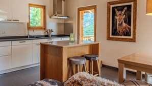 Une cuisine moderne avec des poutres en bois, un îlot central doté de tabourets et un tableau représentant un animal, encadré, accroché au mur.