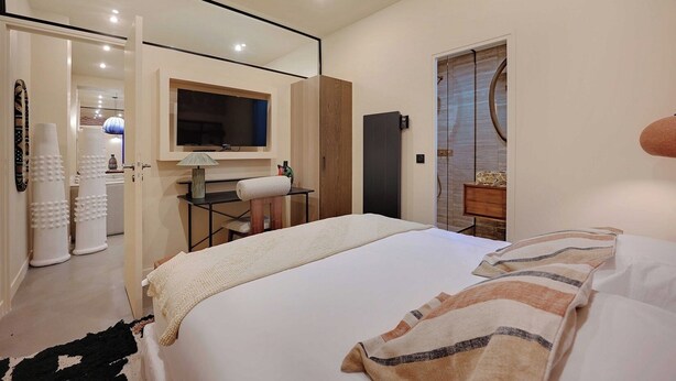 Una habitación de hotel moderna con una cama grande, un escritorio con una silla, un televisor y un armario.