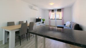 Una sala moderna con comedor, televisor de pantalla plana, planta en maceta y ventana con cortinas.