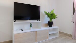 Una sala de estar moderna con un televisor de pantalla plana montado sobre un mueble blanco, una pequeña planta en maceta y un control remoto sobre el mueble.