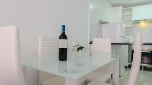 Un comedor moderno con una mesa de vidrio, sillas blancas, una botella de vino y un vaso.