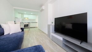 Una sala moderna con un televisor de pantalla plana grande, un sofá azul y una cocina al fondo.