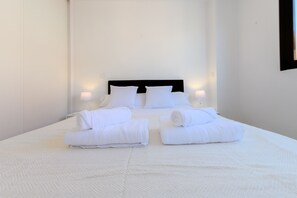 A neatly made bed with white linens and pillows, two bedside lamps, and a clean, white room. - Cozy one bedroom apartment in Chamartin (Madrid)
