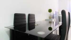 Een moderne vergaderruimte met een glazen tafel, twee zwarte fauteuils, een kleine potplant en een witte plank met een lamp.