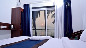 A hotel room with a bed, a desk, a chair, a lamp, and a view of the ocean at sunset. - Sun & Sand Luxury Stays Sea View (Bhatkal)
