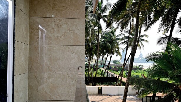 A room with a marble wall and a view of palm trees and a distant building. - Sun & Sand Luxury Stays Sea View (Bhatkal)