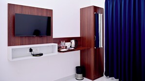 A modern hotel room with a mounted TV, a wooden cabinet, a shelf with toiletries, and a blue curtain. - Sun & Sand Luxury Stays Sea View (Bhatkal)