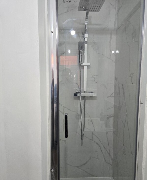 Une douche fermée par des parois en verre, dotée d’un pommeau de douche à main et d’un panneau de commande fixé au mur.