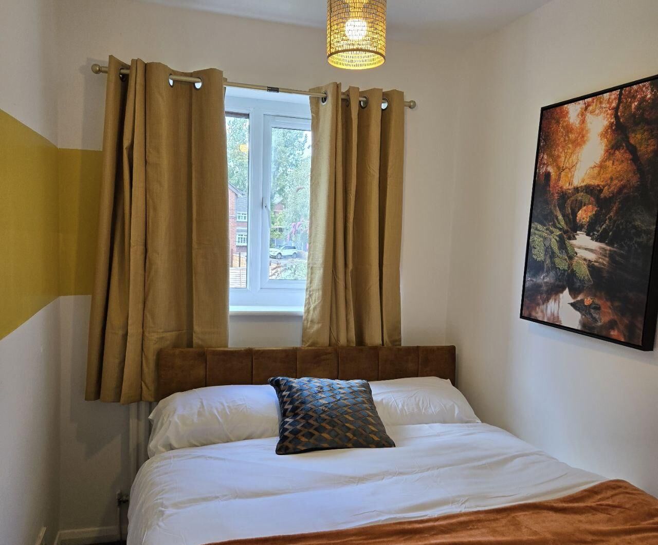 Een slaapkamer met een bed, gordijnen, een raam en een schilderij aan de muur.