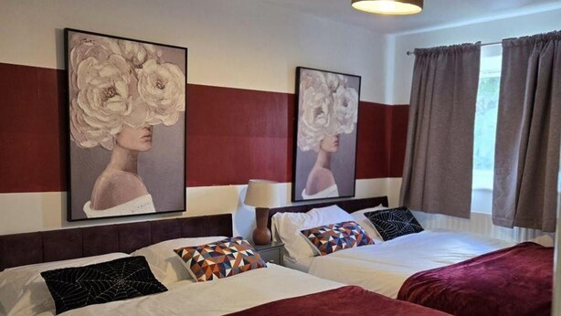 Une chambre d’hôtel avec deux lits, un grand tableau au mur, un lampadaire au plafond et une fenêtre avec des rideaux.