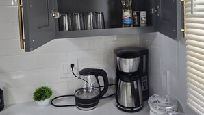 A kitchen with grey cabinets, a coffee maker, a kettle, and a small plant. - 2024 Remodeled 2bedroom in West CLE (Cleveland)