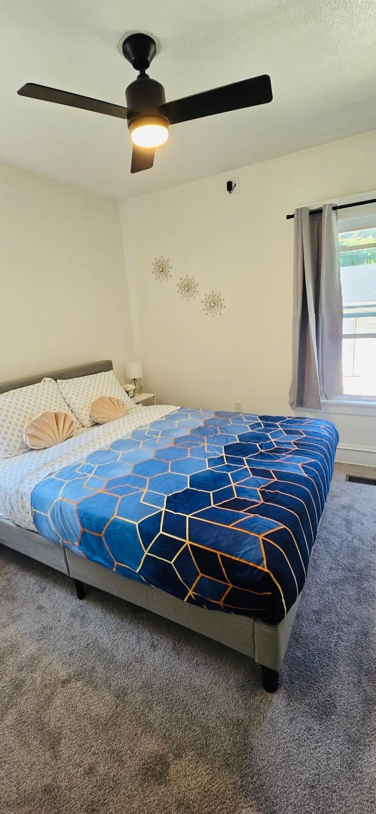 A bedroom with a bed, a ceiling fan, a window with curtains, and wall decorations.