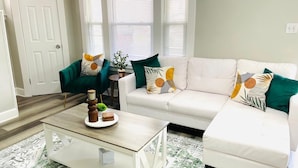 A living room with a white sectional sofa, two green armchairs, a coffee table with decorative items, and a small side table. - Olive and Sunshine CLE House (Cleveland)