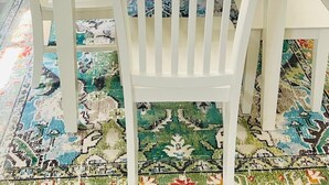 A dining area with a white table set for four, surrounded by white chairs. There are two white shelves on either side of the window, each holding decorative items and small pumpkins. - Olive and Sunshine CLE House (Cleveland)