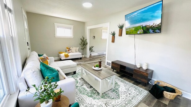 A modern living room with a white sofa, a coffee table, and a TV mounted on the wall. - Olive and Sunshine CLE House (Cleveland)