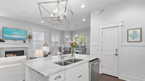 A modern kitchen with a marble countertop, stainless steel sink, and white cabinetry.
