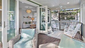 A covered porch with wicker furniture, a white sofa, and a decorative fish wall hanging.