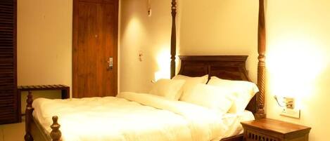 A four-poster bed with a wooden headboard and footboard, a bedside table, and a wooden wardrobe in a hotel room.
