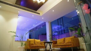 A modern interior with two sofas, a small table, and a large window with a view. - The Vrindwoods (Mathura)